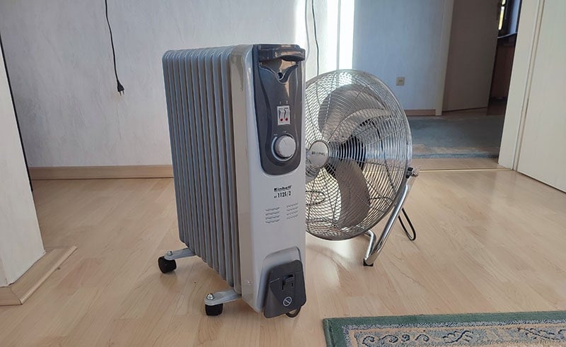 floor fan standing behind oil-filled radiator